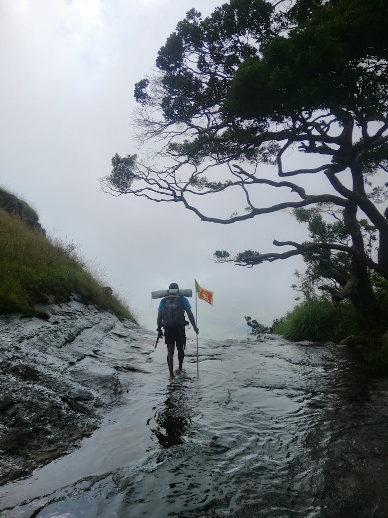 A lone hiker carrying the Sri Lankan flag walks along Dumbaragama stream under a clear sky.