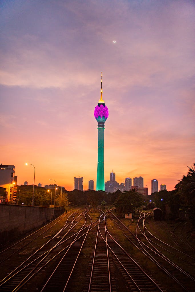 View of illuminated Colombo Lotus Tower at sunset with railway foreground in Sri Lanka.